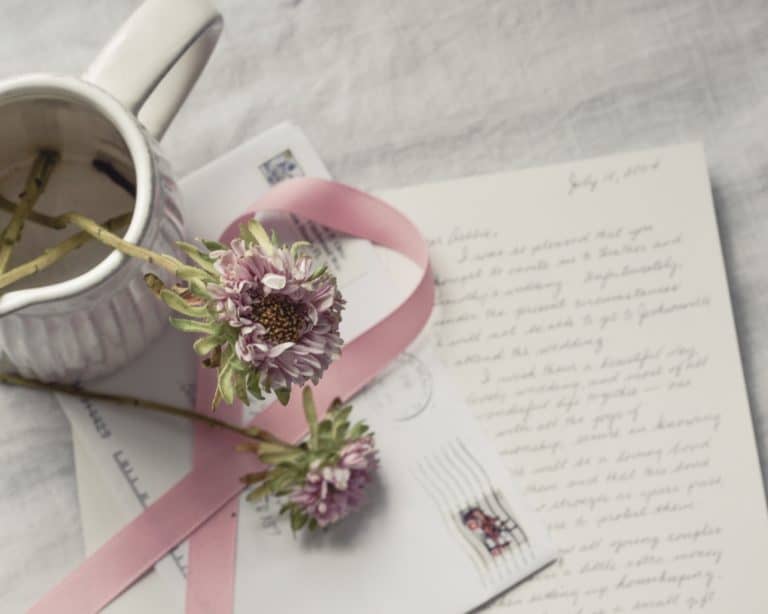 A coffee cup with a ribbon and flowers on a letter